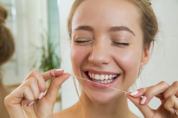 woman holding up floss next to her pearly white smile