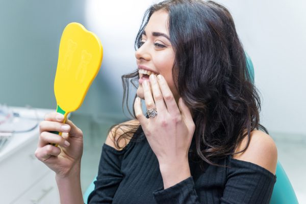 woman looking at her new smile in a handheld mirror