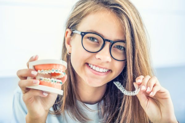 young girl holding up Invisalign and braces