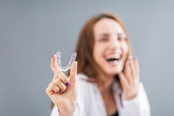 woman smiling while holding her Invisalign tray
